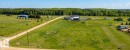 Expansive green acreage with a gravel road, mature treeline, and utility poles - 30 River Ridge Estates, Rural Wetaskiwin County, AB 