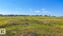 Expansive open land featuring natural grasses and distant structures under a clear sky - 30 River Ridge Estates, Rural Wetaskiwin County, AB 