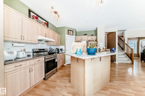 Kitchen with electric stove, a breakfast bar, light wood finished floors, track lighting, and light wood finish cabinets - 4619 151 Avenue Nw, Edmonton, AB - Indoor Photo Showing Kitchen