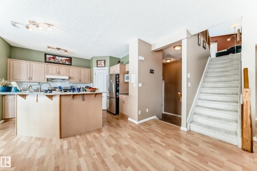 Kitchen featuring a kitchen bar, light wood finish cabinetry, freestanding refrigerator, light wood finished floors, and a textured ceiling - 4619 151 Avenue Nw, Edmonton, AB - Indoor Photo Showing Kitchen