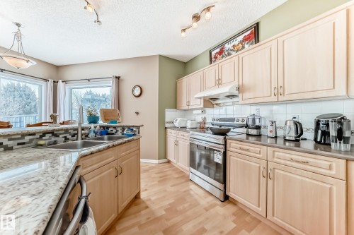 Kitchen featuring stainless steel appliances, light wood finish cabinets, tasteful backsplash, light wood-style flooring, and track lighting - 4619 151 Avenue Nw, Edmonton, AB - Indoor Photo Showing Kitchen With Double Sink