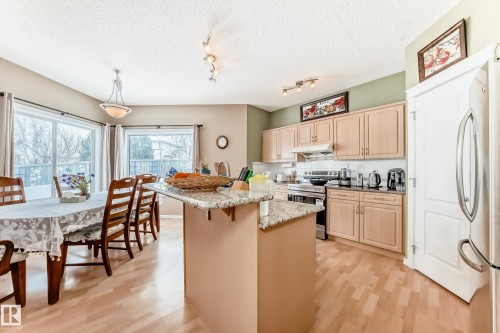 Kitchen with stainless steel appliances, light wood finish cabinetry, backsplash, light wood-style floors, and a textured ceiling - 4619 151 Avenue Nw, Edmonton, AB - Indoor