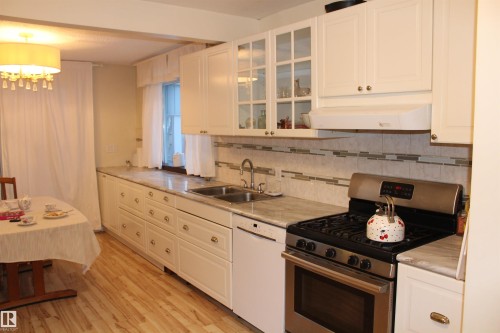 Kitchen featuring stainless steel range with gas stovetop, light countertops, dishwasher, white cabinets, and glass insert cabinets - 12432 134 Street, Edmonton, AB - Indoor Photo Showing Kitchen With Double Sink
