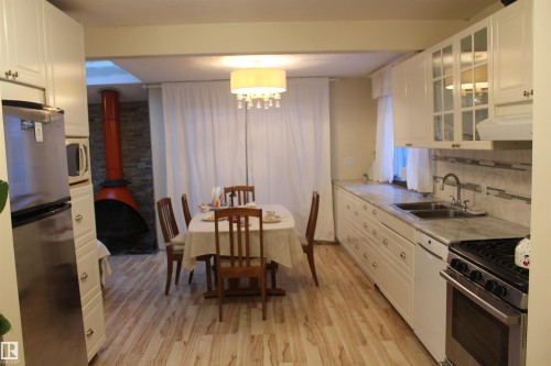 Kitchen with a wood stove, stainless steel appliances, light countertops, white cabinetry, and light wood-style flooring - 12432 134 Street, Edmonton, AB - Indoor