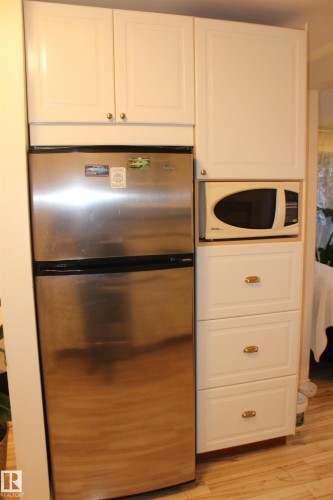 Kitchen featuring freestanding refrigerator, white microwave, light wood finished floors, and white cabinetry - 12432 134 Street, Edmonton, AB - Indoor Photo Showing Kitchen