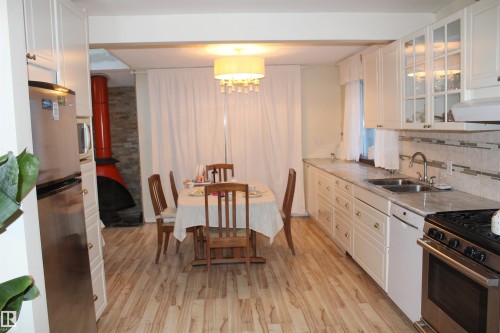 Kitchen with stainless steel appliances, white cabinetry, light countertops, light wood-style floors, and decorative backsplash - 12432 134 Street, Edmonton, AB - Indoor Photo Showing Kitchen With Double Sink