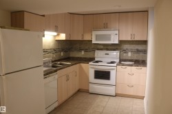 Kitchen featuring white appliances, dark countertops, and light wood finish cabinetry - 