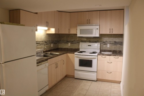 Kitchen featuring white appliances, dark countertops, and light wood finish cabinetry - 12432 134 Street, Edmonton, AB - Indoor Photo Showing Kitchen With Double Sink
