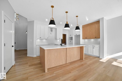 Kitchen featuring a center island with sink, two tone cabinetry, light wood-style flooring, light stone counters, and decorative light fixtures - 523 Ashgrove Circle, Leduc, AB - Indoor Photo Showing Kitchen