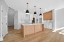 Kitchen featuring a center island with sink, two tone cabinetry, light wood-style flooring, light stone counters, and decorative light fixtures - 523 Ashgrove Circle, Leduc, AB  - Indoor Photo Showing Kitchen 