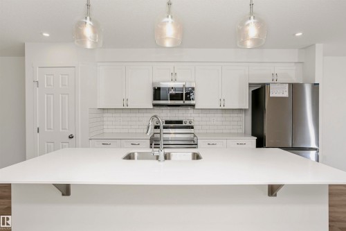 Kitchen with wood finished floors, stainless steel appliances, white cabinets, and a center island with sink - 9552 Carson Bend, Edmonton, AB - Indoor Photo Showing Kitchen With Double Sink With Upgraded Kitchen