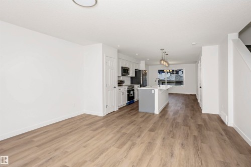 Kitchen with an island with sink, stainless steel appliances, white cabinets, hanging lights, and light wood-style flooring - 9552 Carson Bend, Edmonton, AB - Indoor Photo Showing Kitchen