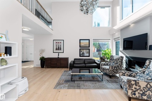 Living area featuring light wood finished floors, a glass covered fireplace, a high ceiling, and a chandelier - 7404 May Common, Edmonton, AB - Indoor Photo Showing Other Room