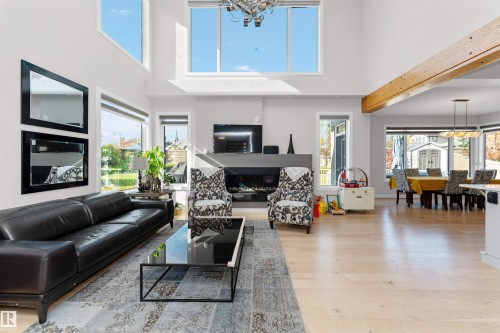 Living area featuring a glass covered fireplace, suspended lighting, light wood finished floors, and a high ceiling - 7404 May Common, Edmonton, AB - Indoor Photo Showing Living Room With Fireplace