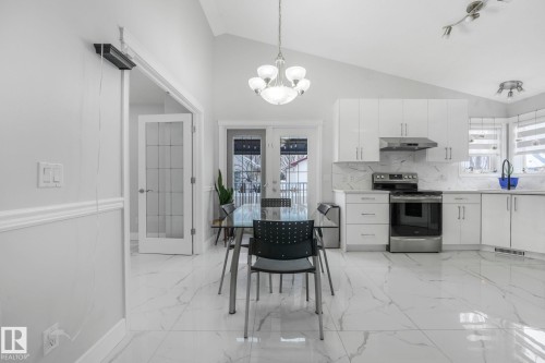 Kitchen featuring stainless steel range with electric cooktop, white cabinetry, hanging lights, plenty of natural light, and vaulted ceiling - 2919 151A Avenue, Edmonton, AB - Indoor Photo Showing Kitchen With Upgraded Kitchen
