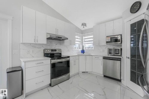 Kitchen featuring lofted ceiling, stainless steel appliances, light marble finish floors, white cabinets, and backsplash - 2919 151A Avenue, Edmonton, AB - Indoor Photo Showing Kitchen With Upgraded Kitchen