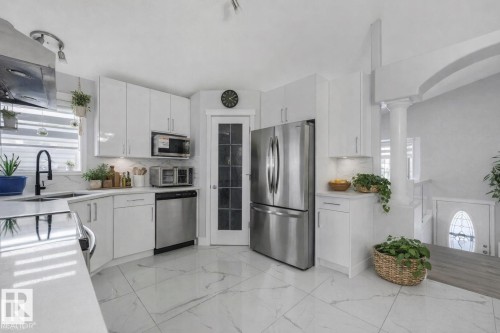 Kitchen with stainless steel appliances, extractor fan, white cabinets, light marble finish flooring, and light stone counters - 2919 151A Avenue, Edmonton, AB - Indoor Photo Showing Kitchen With Upgraded Kitchen