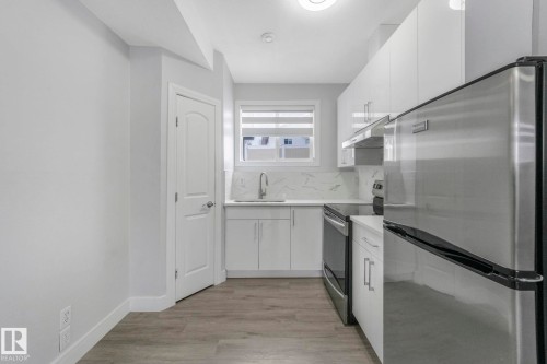 Kitchen featuring stainless steel appliances, white cabinetry, light wood-type flooring, and modern cabinets - 2919 151A Avenue, Edmonton, AB - Indoor Photo Showing Kitchen With Upgraded Kitchen