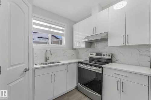 Kitchen featuring stainless steel range with electric stovetop, white cabinetry, backsplash, and light wood-style floors - 2919 151A Avenue, Edmonton, AB - Indoor Photo Showing Kitchen With Double Sink With Upgraded Kitchen