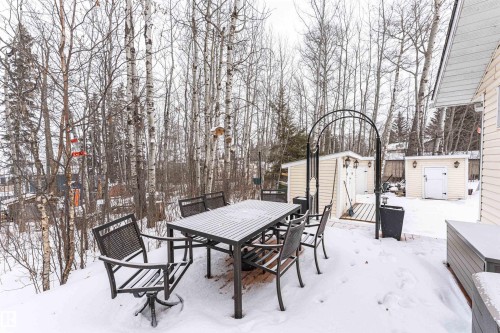 Snow covered patio with a storage unit, a wooden deck, outdoor dining area, and view of scattered trees - 516 5 Street, Rural Lac Ste. Anne County, AB - Outdoor With Deck Patio Veranda