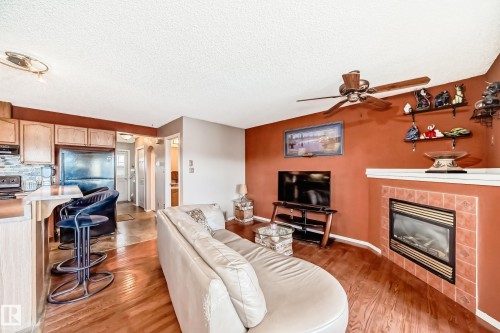 Living room featuring a tile fireplace, a textured ceiling, light wood-style flooring, and a ceiling fan - 2927 30 Street, Edmonton, AB - Indoor Photo Showing Living Room With Fireplace