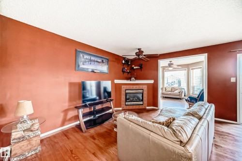 Living area with a tiled fireplace, wood finished floors, a textured ceiling, and a ceiling fan - 2927 30 Street, Edmonton, AB - Indoor Photo Showing Living Room With Fireplace