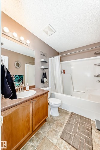 Full bath featuring vanity, shower / bath combo with shower curtain, a textured ceiling, and light tile patterned floors - 2927 30 Street, Edmonton, AB - Indoor Photo Showing Bathroom