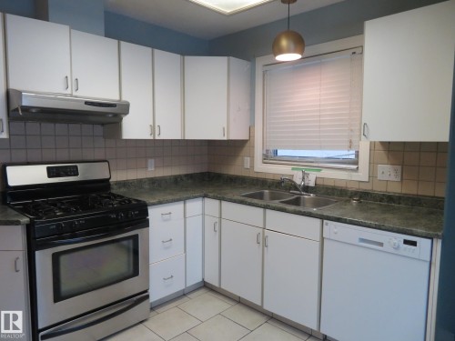 Kitchen with stainless steel gas range oven, dark countertops, dishwasher, white cabinetry, and backsplash - 1855 Mill Woods Road E, Edmonton, AB - Indoor Photo Showing Kitchen With Double Sink