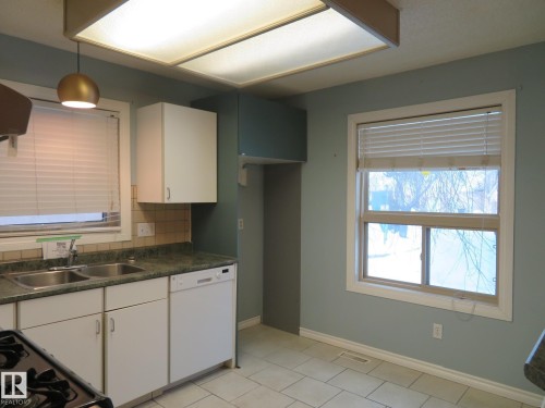 Kitchen featuring dark countertops, white cabinetry, white dishwasher, and backsplash - 1855 Mill Woods Road E, Edmonton, AB - Indoor Photo Showing Kitchen With Double Sink