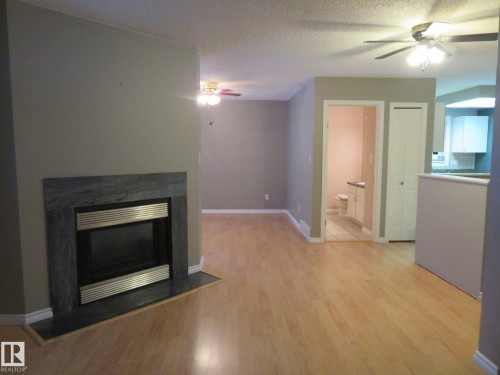 Unfurnished living room with ceiling fan, a glass covered fireplace, light wood-style floors, and a textured ceiling - 1855 Mill Woods Road E, Edmonton, AB - Indoor Photo Showing Living Room With Fireplace