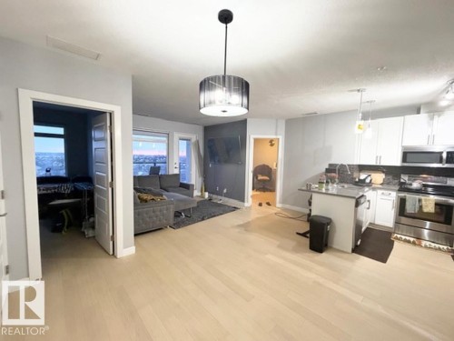 Kitchen featuring stainless steel appliances, a peninsula, white cabinetry, open floor plan, and pendant lighting - 706 5151 Windermere Bv, Edmonton, AB - Indoor Photo Showing Kitchen