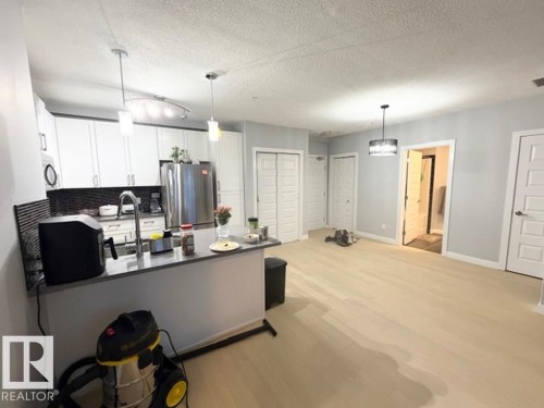 Kitchen with white cabinetry, light wood-style floors, stainless steel appliances, a peninsula, and a textured ceiling - 706 5151 Windermere Bv, Edmonton, AB - Indoor Photo Showing Kitchen