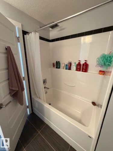 Bathroom featuring a textured ceiling, shower / tub combo, and dark tile patterned flooring - 706 5151 Windermere Bv, Edmonton, AB - Indoor Photo Showing Bathroom