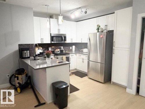 Kitchen featuring stainless steel appliances, white cabinets, a peninsula, a kitchen bar, and a textured ceiling - 706 5151 Windermere Bv, Edmonton, AB - Indoor Photo Showing Kitchen With Upgraded Kitchen