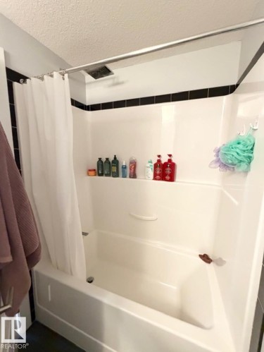 Bathroom with a textured ceiling and shower / tub combo with curtain - 706 5151 Windermere Bv, Edmonton, AB - Indoor Photo Showing Bathroom