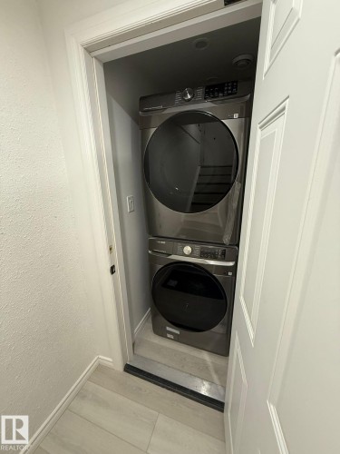 Laundry room featuring stacked washing machine and dryer, a textured wall, and light wood finished floors - 10519 173 Avenue, Edmonton, AB - Indoor Photo Showing Laundry Room