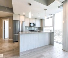 Kitchen featuring modern cabinets, decorative light fixtures, appliances with stainless steel finishes, light stone counters, and light wood-type flooring - 