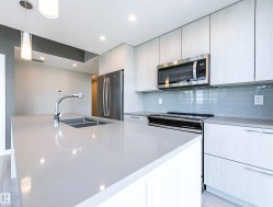 Kitchen with decorative light fixtures, appliances with stainless steel finishes, a center island with sink, tasteful backsplash, and light stone countertops - 