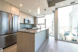 Kitchen with stainless steel appliances, hanging light fixtures, an island with sink, a textured ceiling, and light wood-style flooring - 