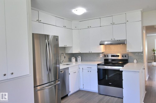 Kitchen featuring stainless steel appliances, vinyl plank flooring, white cabinetry, and tasteful backsplash - 11512 67 Street, Edmonton, AB - Indoor Photo Showing Kitchen With Stainless Steel Kitchen