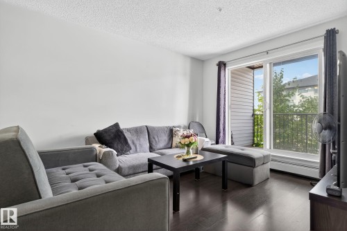 Living room with dark wood finished floors, a textured ceiling, and a baseboard heating unit - 209 3353 16A, Edmonton, AB - Indoor Photo Showing Living Room