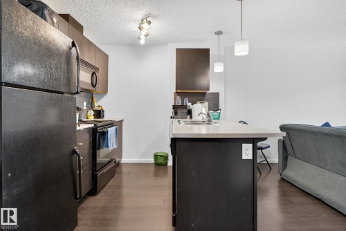 Kitchen with black appliances, open floor plan, dark wood-type flooring, a kitchen breakfast bar, and a textured ceiling - 209 3353 16A, Edmonton, AB - Indoor Photo Showing Kitchen
