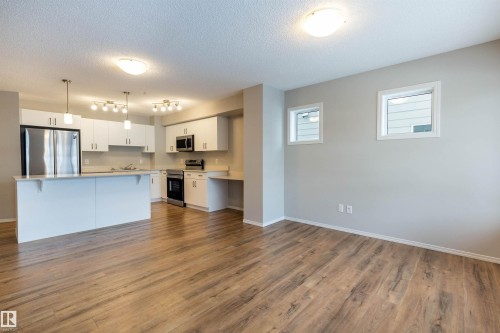 Kitchen with stainless steel appliances, light countertops, white cabinetry, a textured ceiling, and light wood finished floors - 17259 9A Avenue Sw, Edmonton, AB - Indoor Photo Showing Kitchen