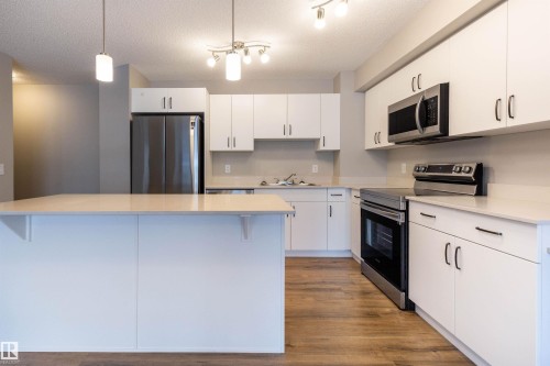 Kitchen featuring stainless steel appliances, decorative light fixtures, white cabinetry, a textured ceiling, and a kitchen island - 17259 9A Avenue Sw, Edmonton, AB - Indoor Photo Showing Kitchen With Stainless Steel Kitchen With Double Sink With Upgraded Kitchen