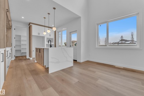 Kitchen featuring a center island with sink, decorative light fixtures, light stone counters, light wood-style floors, and two tone color scheme - 159 Graybriar Dr, Stony Plain, AB - Indoor Photo Showing Kitchen