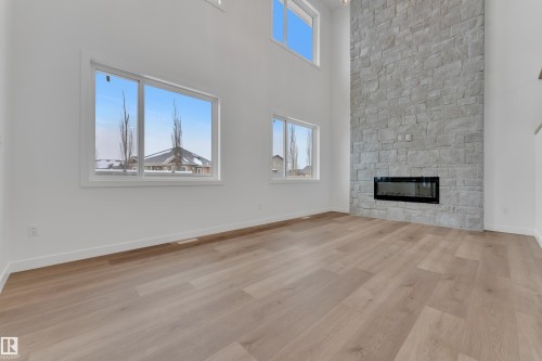 Unfurnished living room with a high ceiling, a stone fireplace, and light wood-type flooring - 159 Graybriar Dr, Stony Plain, AB - Indoor Photo Showing Other Room With Fireplace