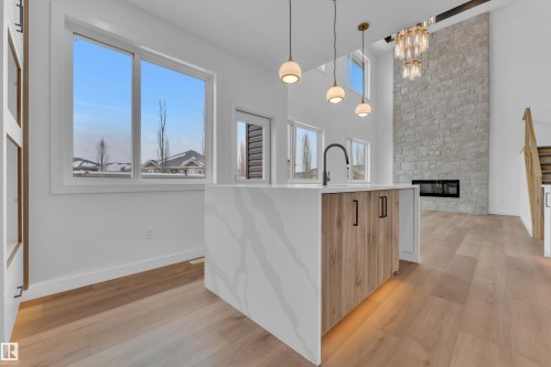 Kitchen with a fireplace, hanging light fixtures, light wood-type flooring, light stone counters, and an island with sink - 159 Graybriar Dr, Stony Plain, AB - Indoor