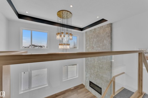 Detailed view of a tray ceiling, wood finished floors, a stone fireplace, and hanging lights - 159 Graybriar Dr, Stony Plain, AB - Indoor Photo Showing Other Room