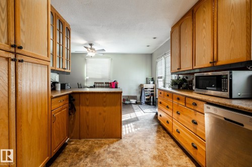 Kitchen featuring a peninsula, stainless steel appliances, glass insert cabinets, wood finish cabinets, and a textured ceiling - 69 Amherst Crescent, St. Albert, AB - Indoor Photo Showing Kitchen