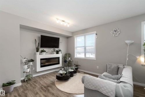 Living room featuring wood finished floors and a glass covered fireplace - 31 2803 James Mowatt Trail, Edmonton, AB - Indoor Photo Showing Living Room With Fireplace